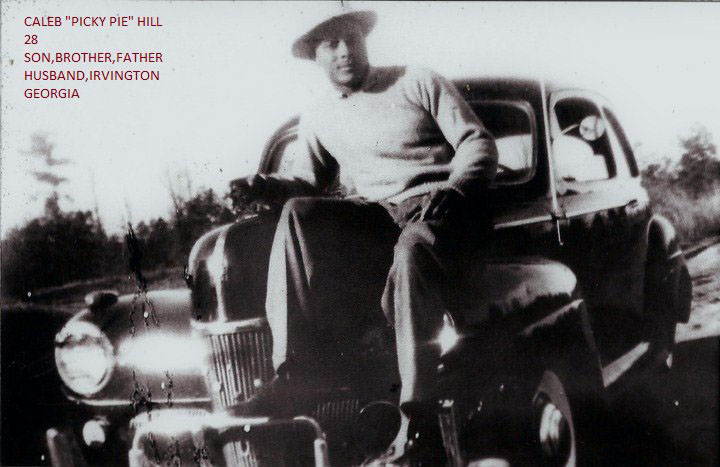 Black and white image of a Black man wearing a hat and sitting on an old car. Text on the photo reads "Caleb "Picky Pie" Hill 28 Son, Brother, Father, Husband, Irvington Georgia"