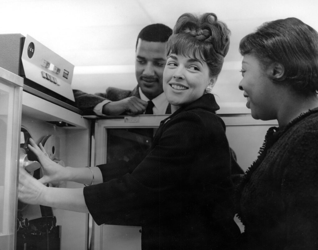 Two unidentified women and one man standing in front of a computer.