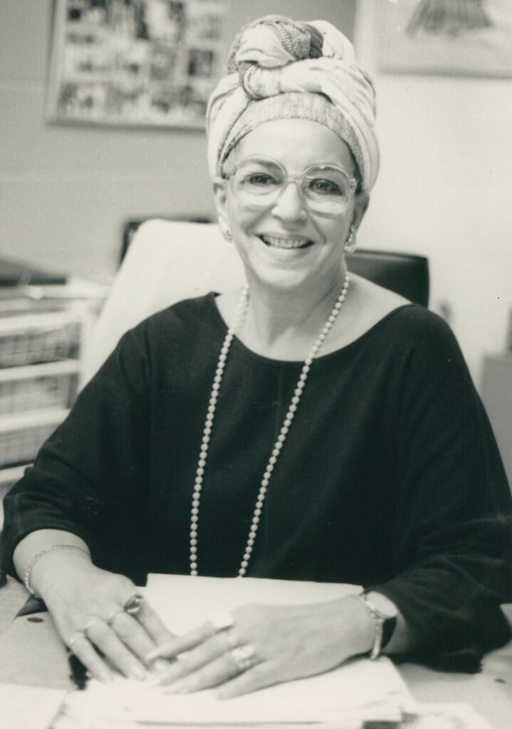 Black and white image of a smiling woman sitting behind a desk
