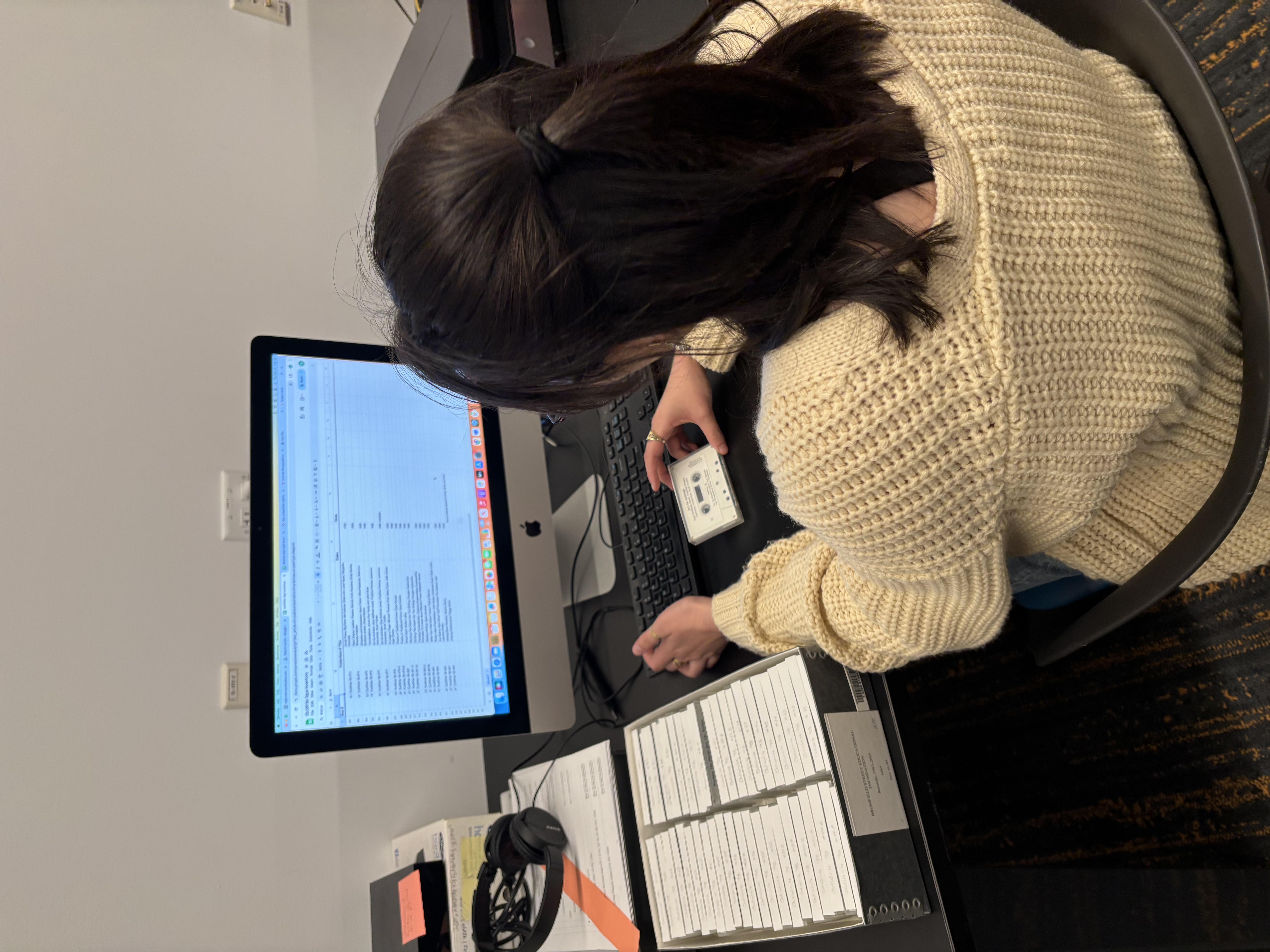 A student sits in front of a computer while holding a white cassette tape