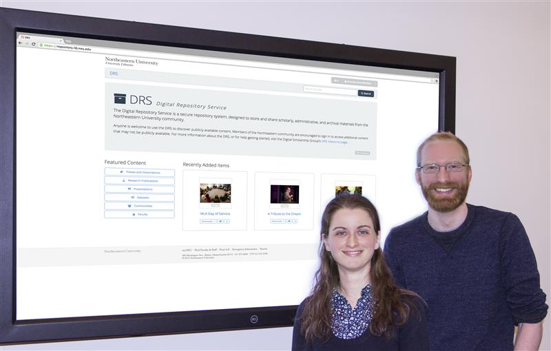 Two people stand in front of a presentation with a screenshot of the DRS behind them
