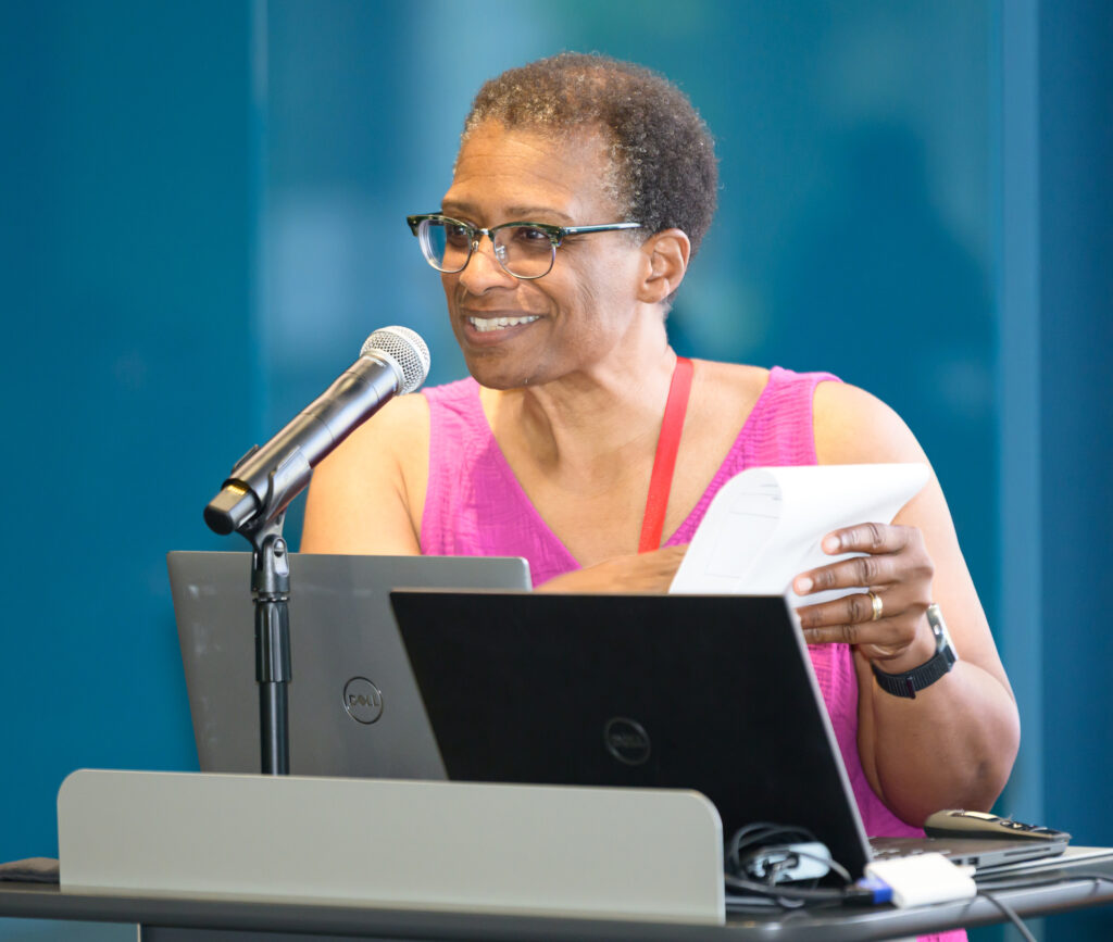 A smiling woman stands behind a podium holding a piece of paper